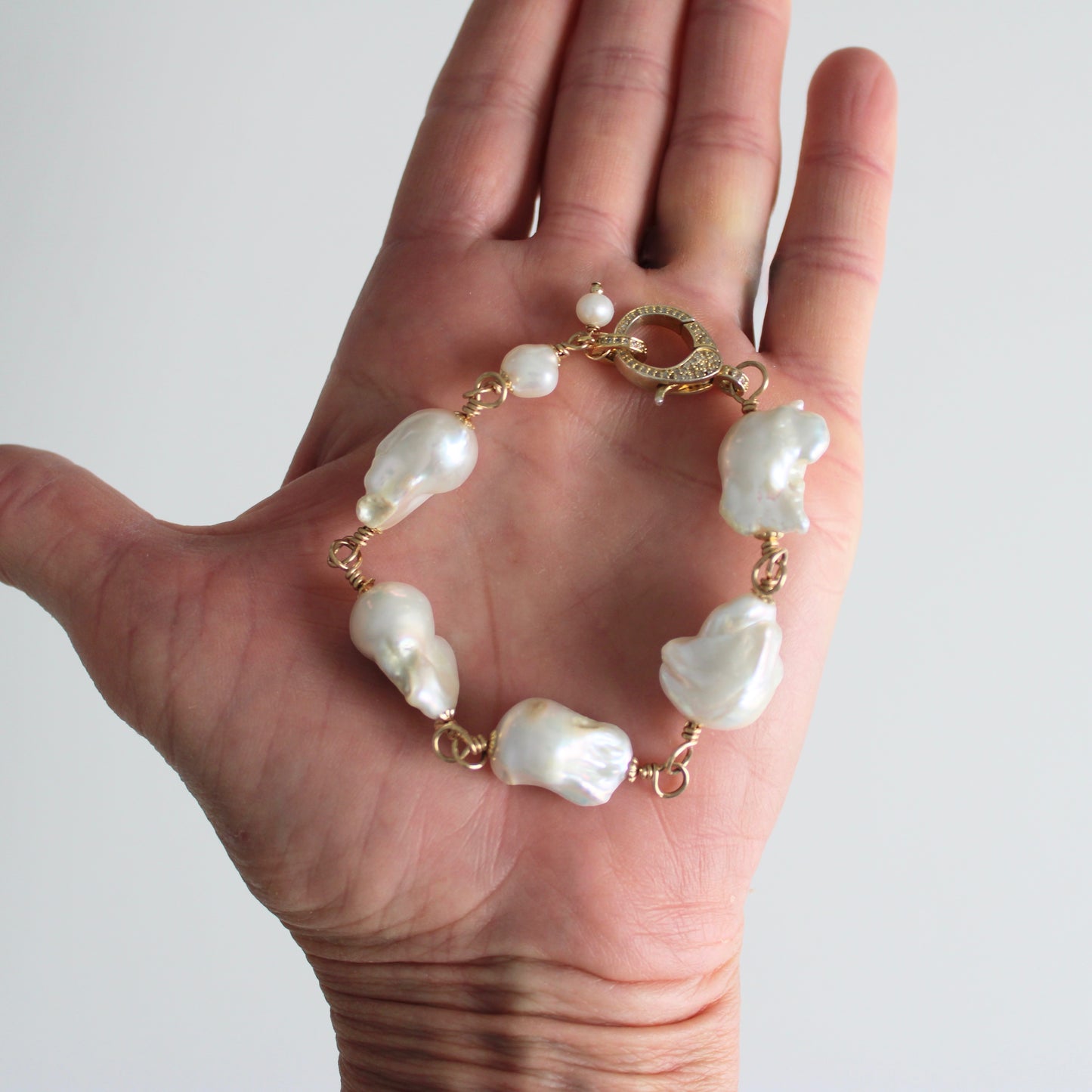 TSJ baroque pearl charm bracelet with gold-tone wire and cubic zirconia clasp on a hand.