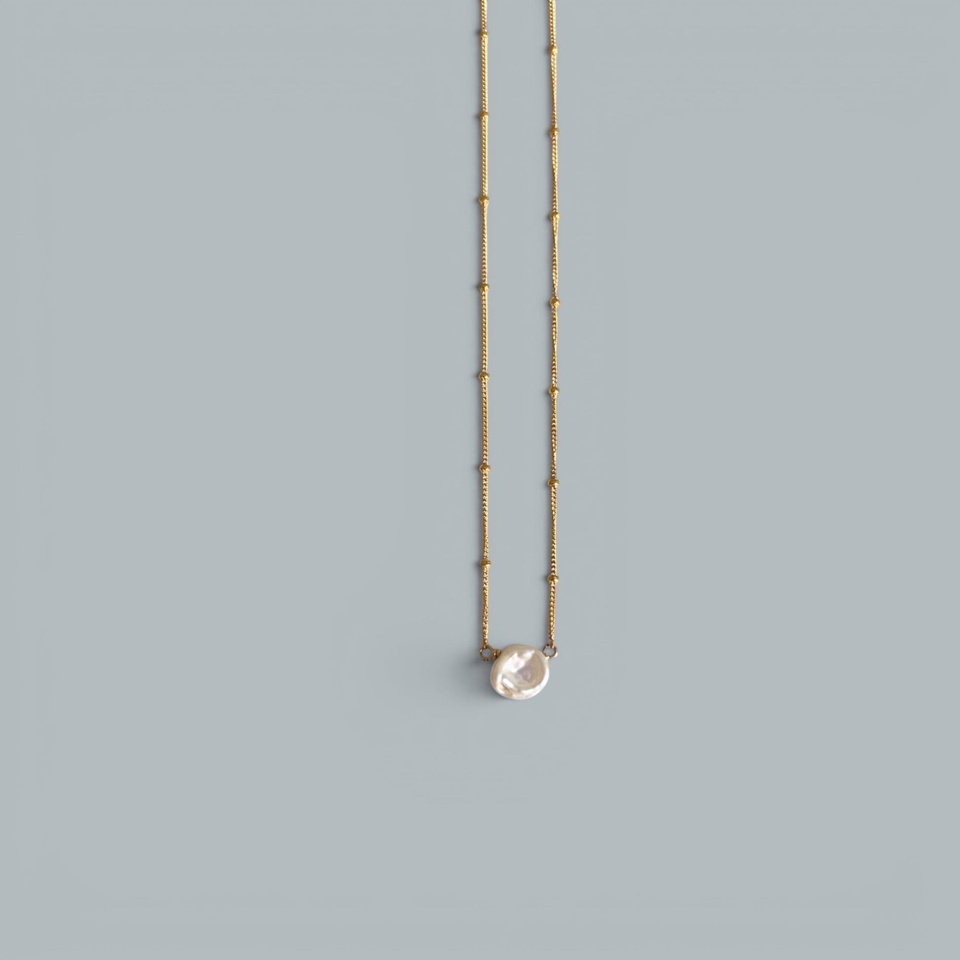 TSJ gold-tone chain necklace with a single, irregular baroque pearl pendant. Minimalist and elegant.